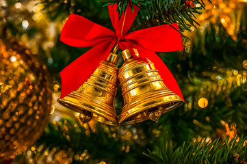 Golden bells with red ribbon hanging on ornamented Christmas tree.