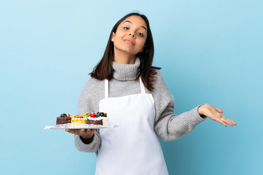 Pastry chef holding a big cake over isolated blue background having doubts. - Powered by Adobe