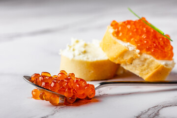 Metal spoon with caviar and bread slice on marble table