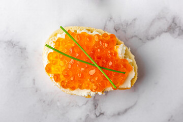 Slice of baguette with red caviar and cream cheese on marble surface