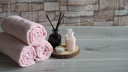 Fotobehang Badkamer Rolled pink towels with aroma diffuser, scented candle, and small lotion bottles on wooden background create a relaxing spa atmosphere. Perfect for wellness, aromatherapy, beauty, and self-care themes  © kanjana