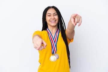Teenager girl with braids and medals over isolated pink background points finger at you while...