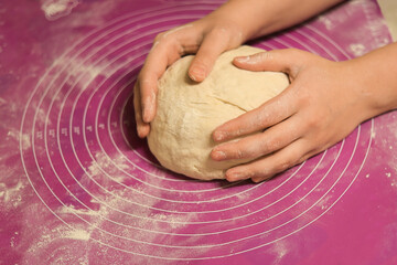 A close-up of hands gently shaping and rounding a large ball of fresh dough on a pink, flour-dusted silicone baking mat.