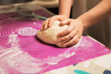 A close-up of hands firmly rolling and shaping a fresh ball of dough on a pink, flour-dusted silicone baking mat.