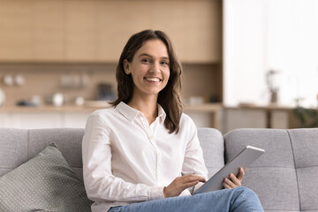 Young woman posing on sofa looking at camera holding tablet