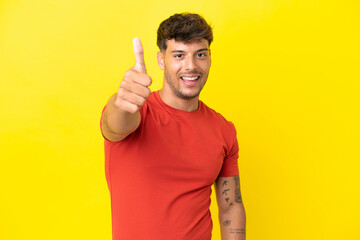 Young caucasian handsome man isolated on yellow background with thumbs up because something good...