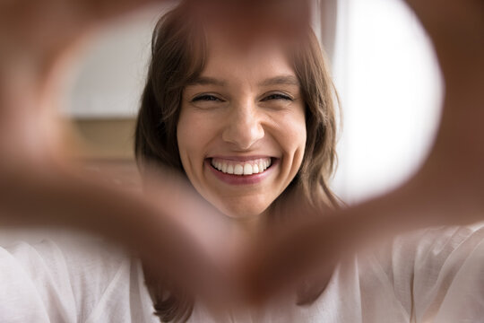 Cheerful young female looking at web camera through finger heart