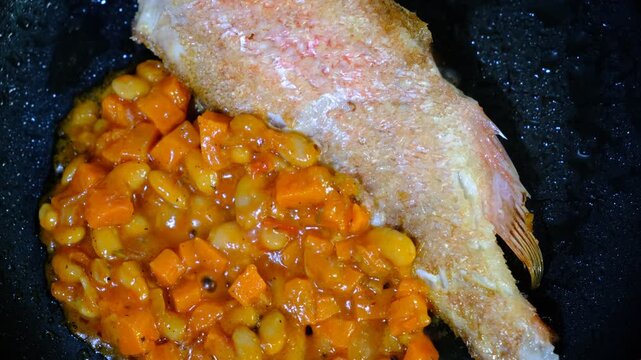 Red sea perch fish with vegetables stew on cooking pan. Cooked with vegetables in samfaina, with tangy tomato caper sauce in a pan. Traditional recipe of Mediterranean gastronomy.