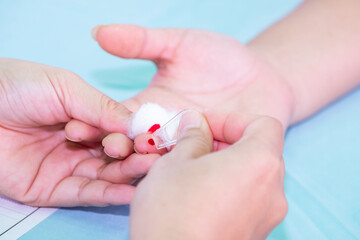 Close up of a healthcare professional using a lancet to prick a patient’s fingertip for a blood test. Medical procedure for glucose check, diabetes test, or health examination in clinic.