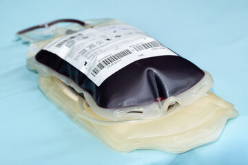 Close up of a blood donation bag filled with human blood placed on a blue background, showing barcode and label details, representing healthcare, transfusion, and medical donation concepts.