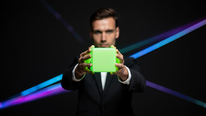 A man in a suit holding a bright green cube with abstract light streaks in the background.