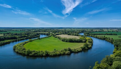 Obraz premium Serene aerial vista captures a winding blue river flowing through lush green fields and vibrant forests under a clear, cloud-dappled sky