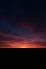 Obraz premium Dramatic twilight sky painted with vibrant crimson and deep indigo clouds over a silhouetted treeline, evoking a sense of serene beauty and natural wonder.