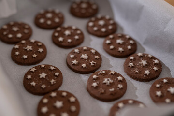 Chocolate cookies with white star decorations baking on parchment paper