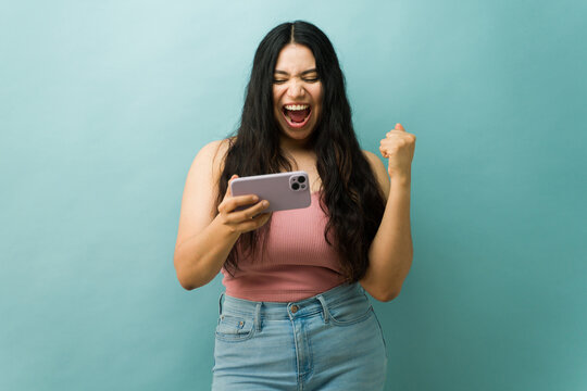 Fototapeta Young woman celebrating victory playing mobile game