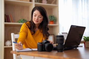 Woman photographer working on laptop and writing notes