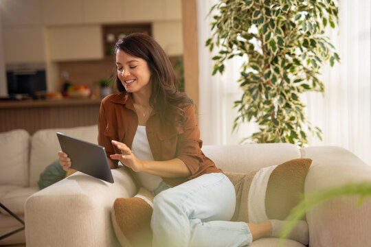 Woman relaxing at home browsing online content on tablet - Powered by Adobe