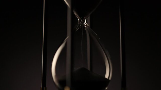 dark sand flowing through a transparent hourglass, symbolizing the quiet passage of time