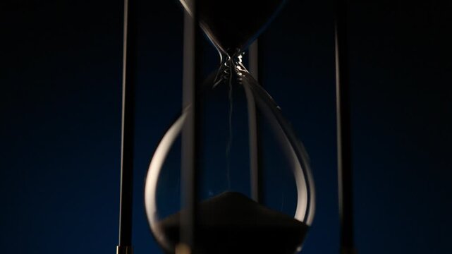 macro cinematic shot of black sand running smoothly in an hourglass, symbol of time, patience, and inevitable change.