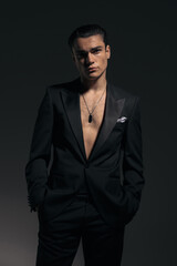 elegant young man in black tuxedo with no shirt holding hands in pockets