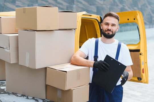 Deliveryman holding clipboard near cardboard boxes and van