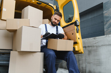 Delivery man checking packages list sitting in van with cardboard boxes
