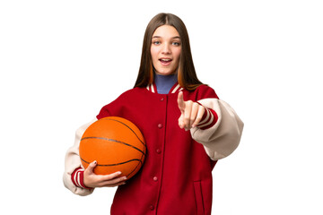 Teenager girl playing basketball over isolated chroma key background surprised and pointing front