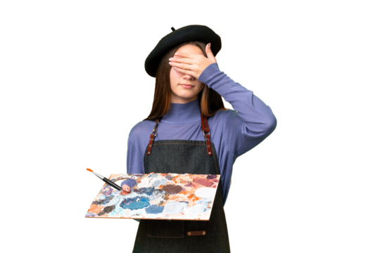 Young artist man holding a palette over isolated chroma key background covering eyes by hands. Do not want to see something