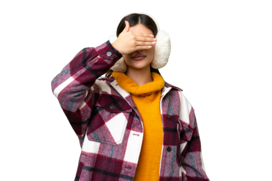 Young Russian woman wearing winter muffs over isolated chroma key background covering eyes by hands. Do not want to see something