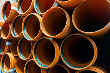 Stacked orange pipes in a construction site showing different sizes and shapes for plumbing and...