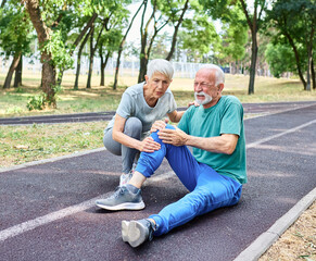 Active mid age mature couple jogging together, helping and supporting each other with a injury problem  in the park