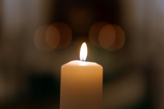 Single burning candle with soft bokeh lights — peaceful warm flame symbolizing prayer, remembrance, faith and hope in dark background