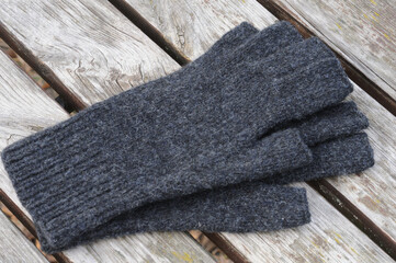 Woolen gray gloves with open fingers on a wooden background. Top view.