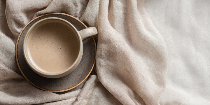 Minimalist beige ceramic coffee cup on linen fabric in soft natural light