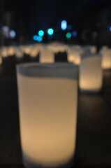 Close-up of a frosted glass votive candle holder with a soft glow in a dark room with blurred background lights.