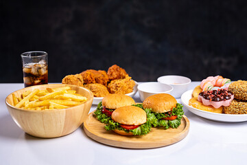 French fries, burgers and other fast food on plate on wooden table against black background, studio shot, unhealthy fast food