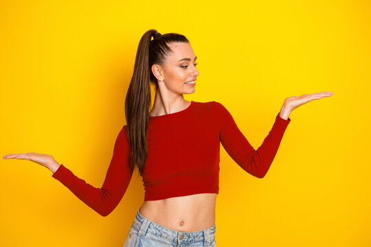 Fototapeta Young woman in red crop top poses with outstretched hands against yellow background promoting fashion lifestyle
