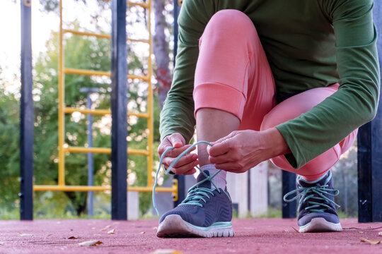 Close-up of a senior woman tying her sports shoes before exercising at an outdoor park, dressed in bright sportswear during a morning fitness routine.
