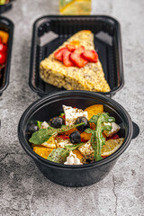 Healthy salad with feta cheese, olives, arugula, and orange slices served in black plastic container