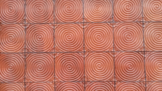 Texture of terracotta or cement tile in reddish-brown color with a spiral circle pattern.