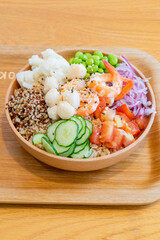 A gourmet poke bowl featuring scallops, shrimp, potato, cucumber, and quinoa rice, drizzled with parmesan cheese dressing and mustard vinaigrette. The dish presents a refreshing summer flavor with a b