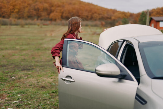 A candid scene of a woman inspecting her car with the hood open on a rural roadside, conveying authentic problem-solving and trustworthy self-reliance in a natural setting, аутентичность.