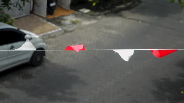 Footage captures triangular red and white flags fluttering on a string outdoors, creating a festive atmosphere, with a car parked nearby, adding a touch of urban celebration.