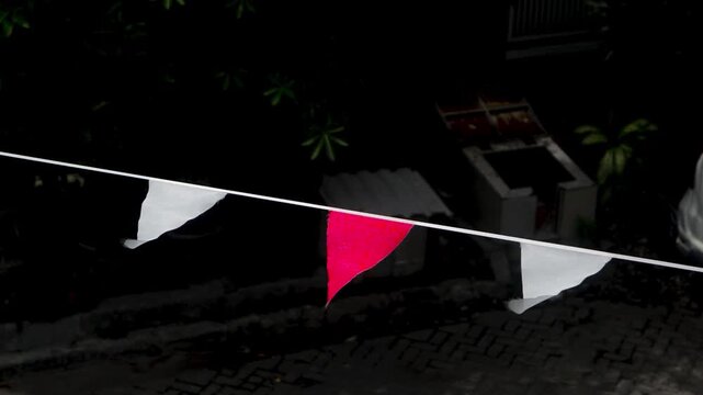 This footage shows a string of alternating red and white triangular flags hanging outdoors at night, gently swaying in the breeze, adding a festive touch to the surroundings.