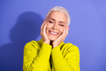 Smiling mature woman with short white hair in a bright yellow sweater enjoying happiness against a purple background for lifestyle wellness