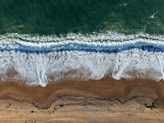 Aerial Top view of a transparent blue sea with beautiful waves at sunny day in summer. Tropical landscape from the air of ocean with azure water, sandy bottom at sunset. Aerial view of sand beach.