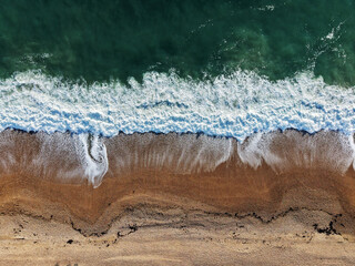 Aerial Top view of a transparent blue sea with beautiful waves at sunny day in summer. Tropical landscape from the air of ocean with azure water, sandy bottom at sunset. Aerial view of sand beach.