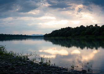 Fototapeta premium Landscape of Sava river and mountain in distance during sunset, glow in clouds reflecting in water surface