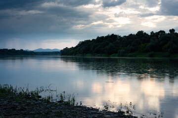 Rainfall over river during dusk, water drips glowing, forest on riverbank and mountain in distance