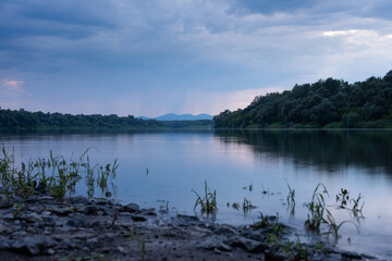 Landscape with river Sava and mountain in background during heavy rainfall, gloomy clouds reflecting in water surface